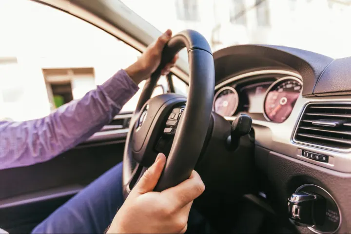 A close-up of a driver holding a steering wheel inside a modern vehicle, suggesting early symptoms of a bad body control module affecting car electronics.