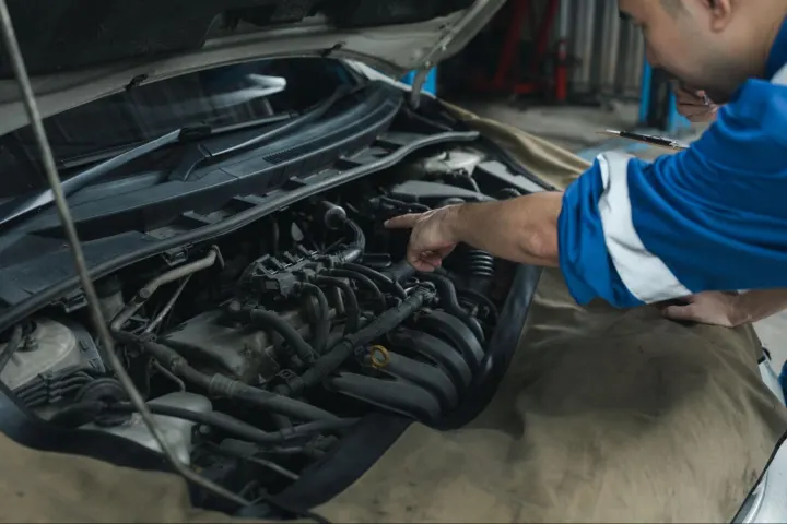 Technician is pointing inside an open car engine bay while inspecting the engine control computer