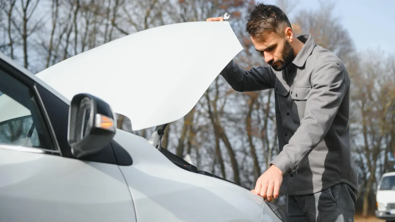 A man examines his car’s engine on the roadside, showing frustration caused by impaired powertrain function.
