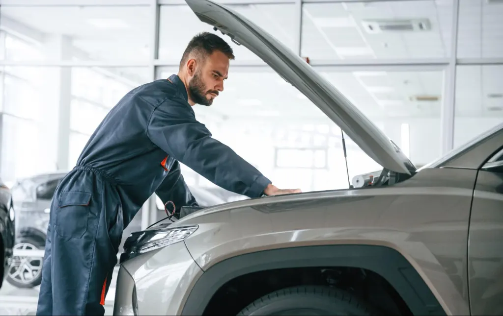 A man examines his car’s engine on the roadside, showing frustration caused by impaired powertrain function.