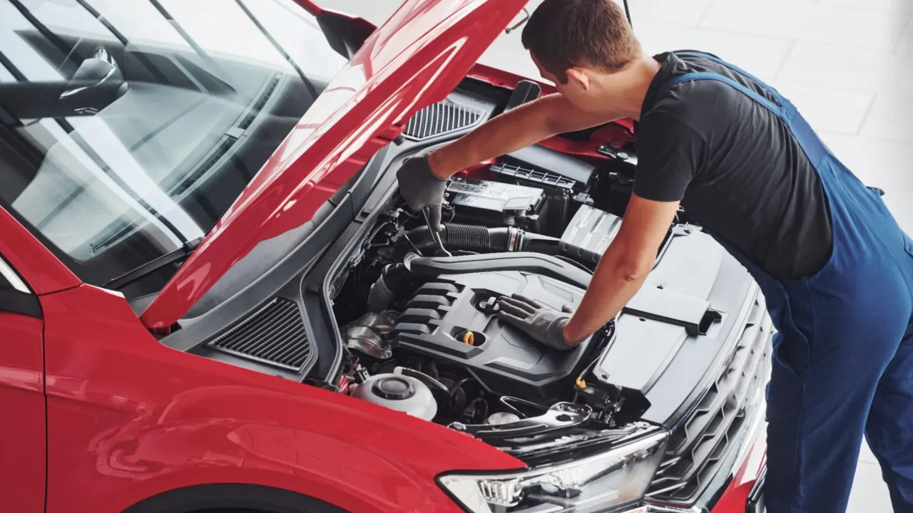 Professional technician using tools to test ECM inputs and outputs under the hood of a red car for accurate engine diagnostics.