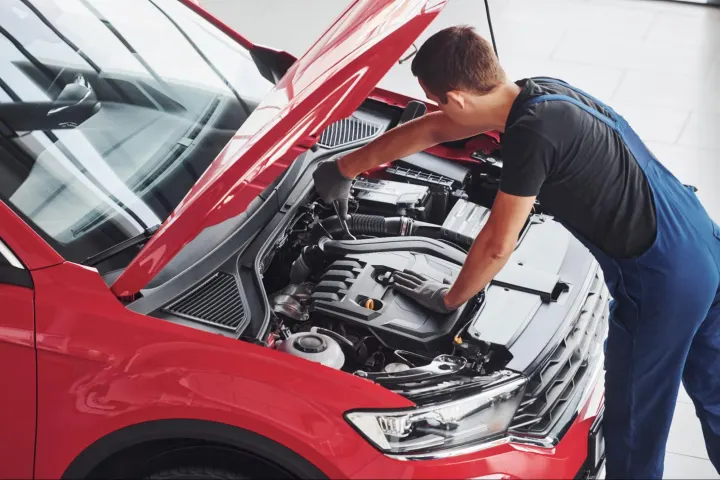 Professional technician using tools to test ECM inputs and outputs under the hood of a red car for accurate engine diagnostics.